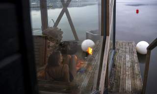 Kvinne sitter i en flytende badstu og ser utover vannet