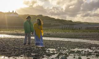 A couple stand on the rocky shore at Cuckmere Haven near Seaford Head, Sussex