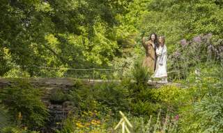 Two women stand on a bridge taking a selfie, in Wakehurst gardens in Sussex