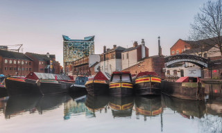 Canal boats moored at Gas Street Basin Birmingham in front of bring building a a large cubed glass building behind
