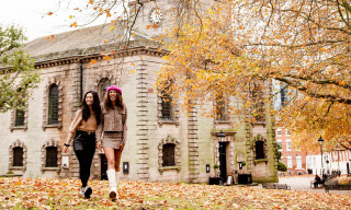 Two friends walking through a park in autumn with fallen orange and red leaves with St Phillip's Cathedral in the background