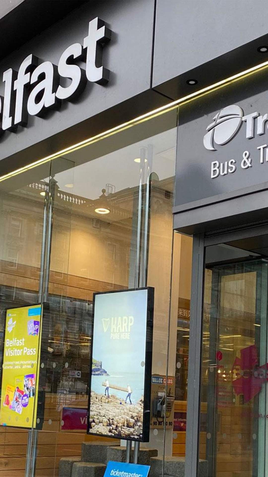 An exterior of the Belfast Welcome Centre with a tourist using a touch screen inside.