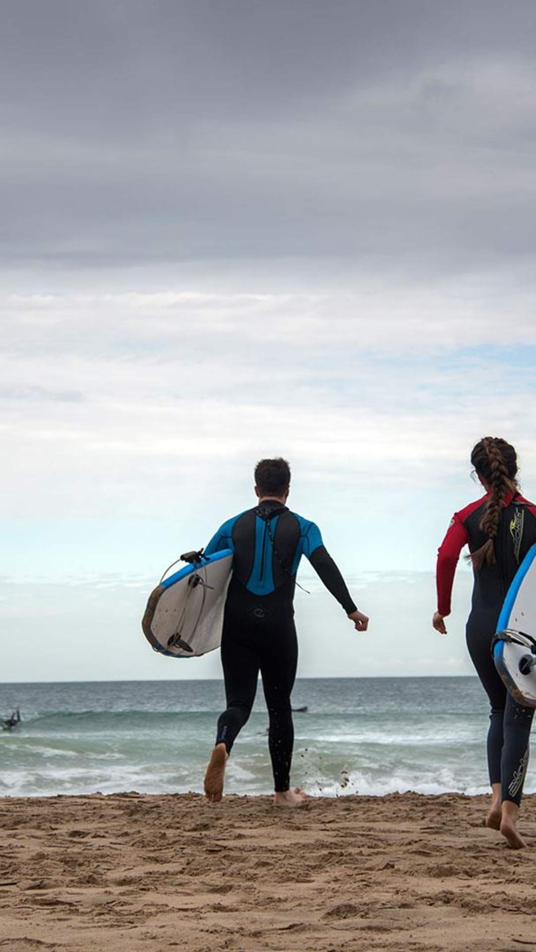 Four surfers running towards the sea to go Surfing at Whiterocks Beach, Portrush, County Antrim
