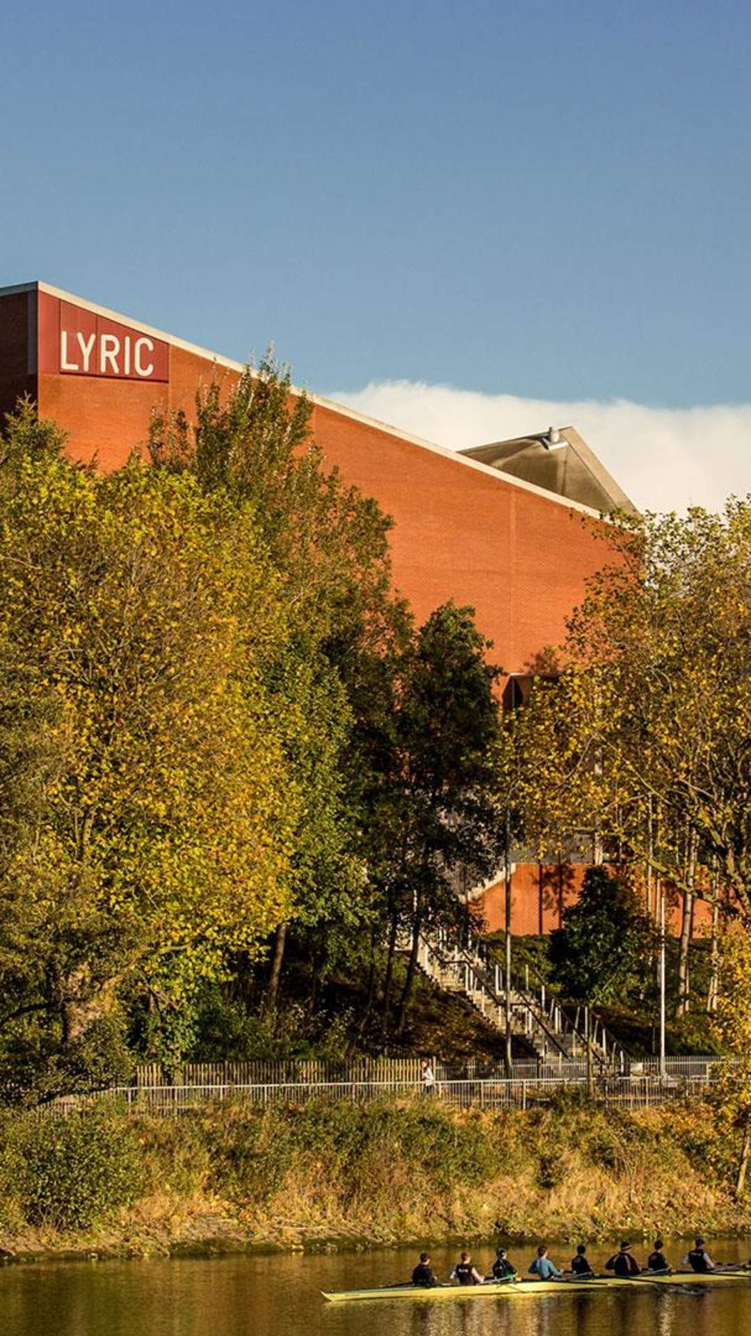 Exterior of The Lyric Theatre in Belfast on a sunny day with rowers on the river beside it