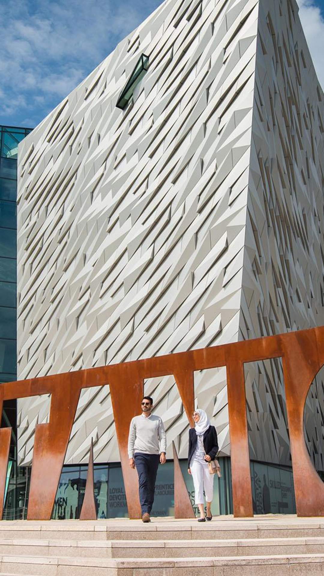 External Image of a couple visiting Titanic Belfast, at the Titanic Belfast sign.