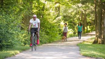 Man riding bike and women walking along wooded rail trail