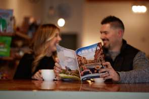 Two people sitting in a coffee shop, drinking out of mugs and holding a Galena Country Visitor's Guide.