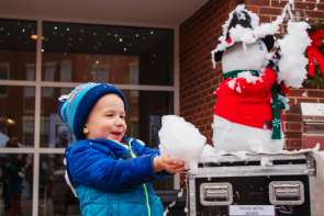 Child holding snow, standing outside a brick building.