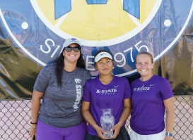 Three members of the Kansas State women’s tennis team pose together, with the player in the center holding a trophy at the Milwaukee Tennis Classic.