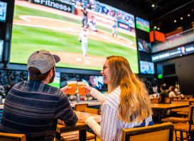 couple cheersing beer at bar with baseball on tv