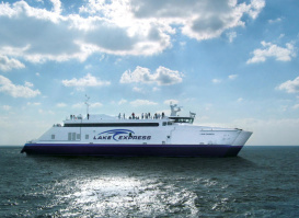 The Lake Express high-speed ferry crossing Lake Michigan on a sunny day, with passengers standing on the upper deck under a partly cloudy sky.