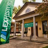 A yellow building with columns and a green sign that says LEX History