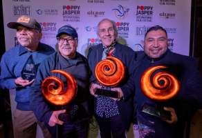 Four men holding orange swirl-shaped awards in front of a Poppy Jasper Film Festival labeled backdrop
