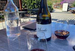 Wine bottle and glasses on a table with blue sky in the background at Sarah's Vineyard