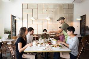 Man Serving Food To 3 People At A Table In Laziz Kitchen