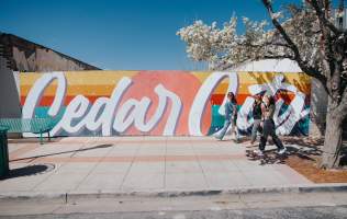 Brightly colored mural saying "Cedar City" with three women walking and blossoms on the trees framing either side.