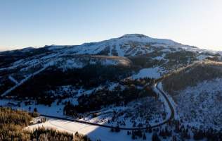 Aerial view of a snow covered mountain with ski resort lifts and runs on the mountain side, visible in a blanket of snow.