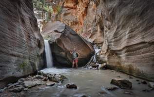 Woman standing beside a waterfall within a red rock slot canyon in southern Utah.