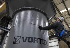 A worker inside a shop touching a piece of equipment with the name "Vortex" on it.