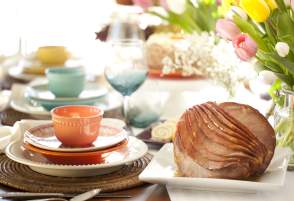 Easter Ham Sitting on Table Decorated With Colorful Dish Sets and Tulips