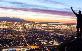 Man with hands raised looking out over the Salt Lake Valley at sunset