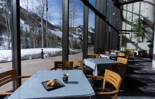 Tables and chairs in front of floor to ceiling windows looking out on a snow covered mountainside at Snowbird