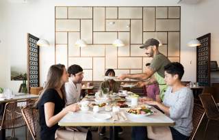 Man Serving Food To 3 People At A Table In Laziz Kitchen