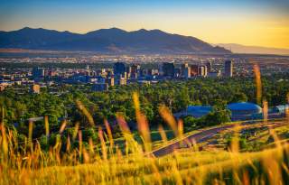 Scenic view of Salt Lake with wild summer grass in the foreground then green trees, then the city  with the mountains and golden light in the background