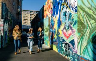 3 girls walking in sunlit alley with murals