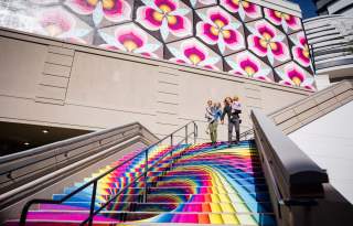 Family on stairs that are painted in a rainbow swirl with cherry blossoms on the wall behind them