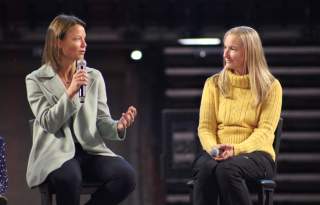 2 women sitting on a stage talking to each other