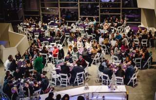 large group of people seated at round tables with a bar service in the foreground