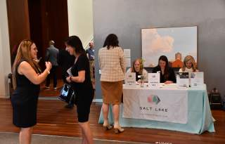 2 women in foreground chatting happily, 4 women in the background at a registration table
