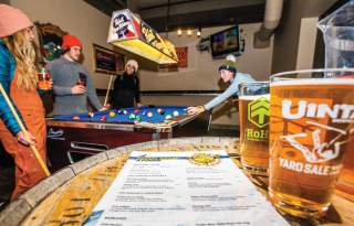 Glass of Uintah beer and menu with skiers holding pool cues and playing pool