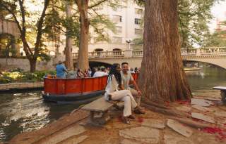 Couple sitting on bench at the River Walk in front of Go Rio RIver Cruise barge