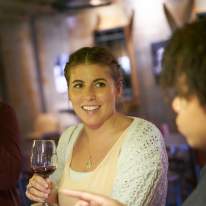 Woman in Sweater Smiling at a Friend with a Glass of Wine in Hand