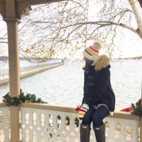 girl staring out at lake in winter gear during the christmas season while sitting on a gazebo