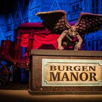 a gargoyle on a sign for Burgen Manor with red and blue stage lighting backdrop