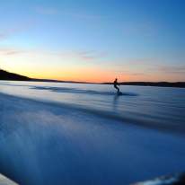 a sunset over a lake with someone wake boarding
