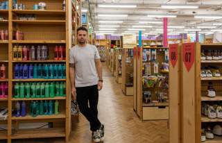 Manchester based artist, Corbin, leaning against a shelf full of different coloured paints in his shop.