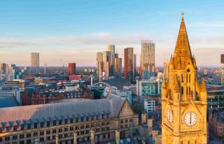 Manchester skyline at sunset featuring Beetham Tower, the modern high-rises of Deansgate Square, Manchester Central, and the illuminated clock tower of Manchester Town Hall Annex in the foreground.