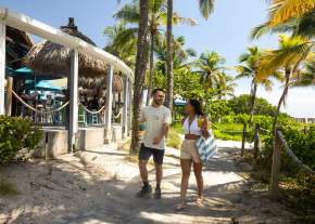 A couple walking on the path between Lucky Fish and the beach, ready to spend some time in the sand at Pompano Beach, FL