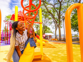 mom helping daughter swing on monkey bars