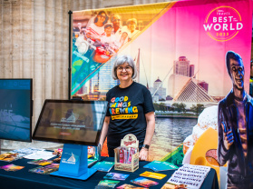smiling volunteer stands by Visit Milwaukee display at union station
