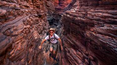 A man looks towards the camera as he traverses Spiderwalk in Karijini National Park, using his hands and feet along narrow rock ledges.