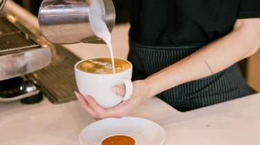 Milk artfully being poured into coffee to create a leaf shape.