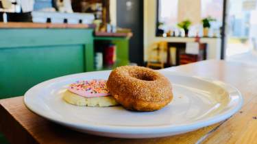 A cinnamon sugar donut and frosted sugar cookie sitting on a white plate in Mud Pie Bakery & Coffee