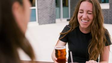 Girls laughing over drinks at an outside picnic table at Strang Hall.