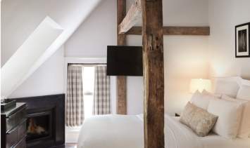 A guest room at the Bedford Post Inn. The room has wooden beams going over the bed and a fireplace can be seen in the background.