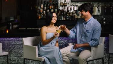 A couple sitting in front of the bar at the White House Hotel, clinking their drink glasses.